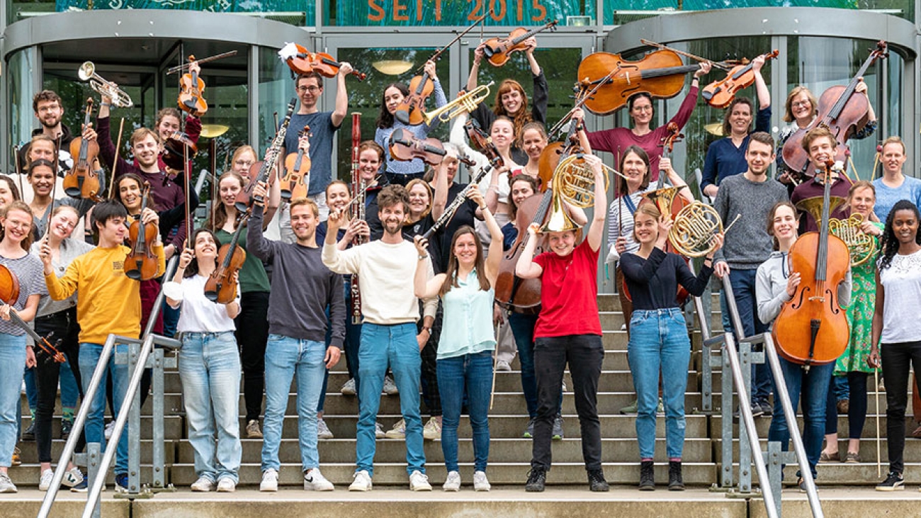 Ein Orchester hält die Instrumente hoch und steht auf einer Treppe.