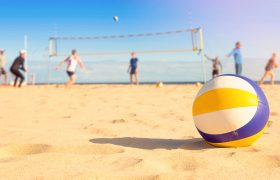Ein Volleyball liegt im Sand, im Hintergrund wird gespielt.