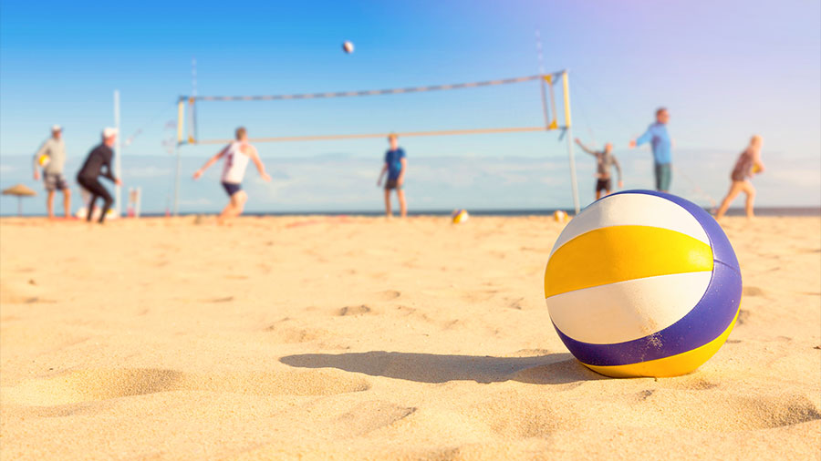 Ein Volleyball liegt im Sand, im Hintergrund wird gespielt.