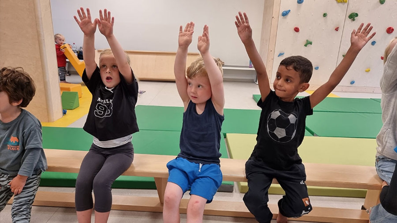 Kinder sitzen auf einer Bank und heben die Hände.